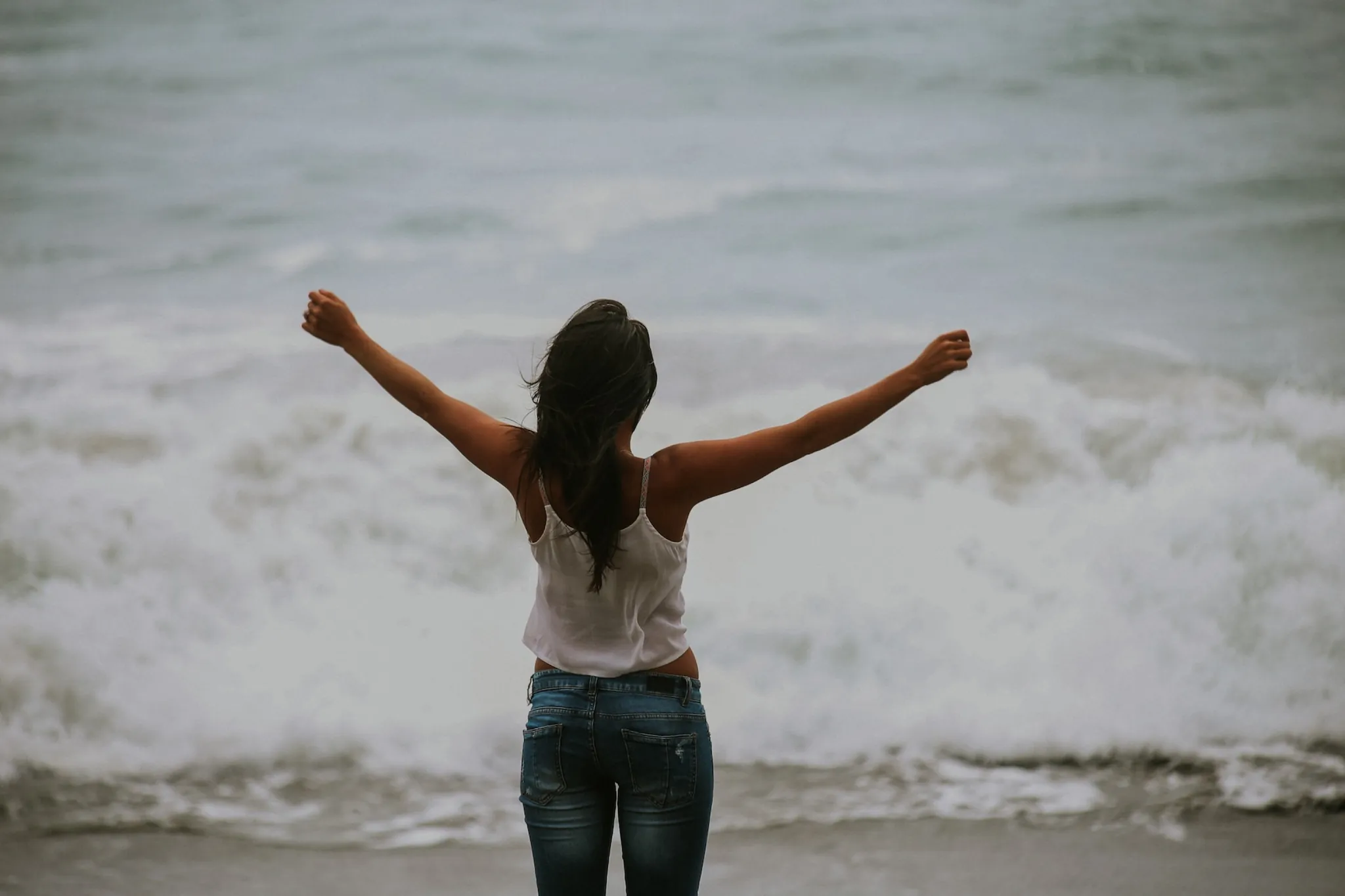 A woman with her arms raised facing the surf