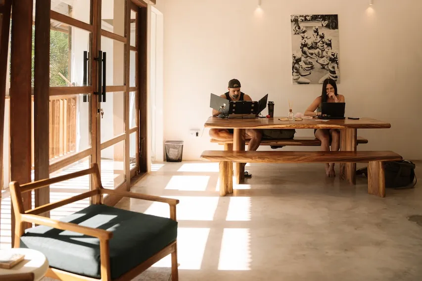 Two members working on laptops at the long teak table in ELEMNT's coworking room, Uluwatu