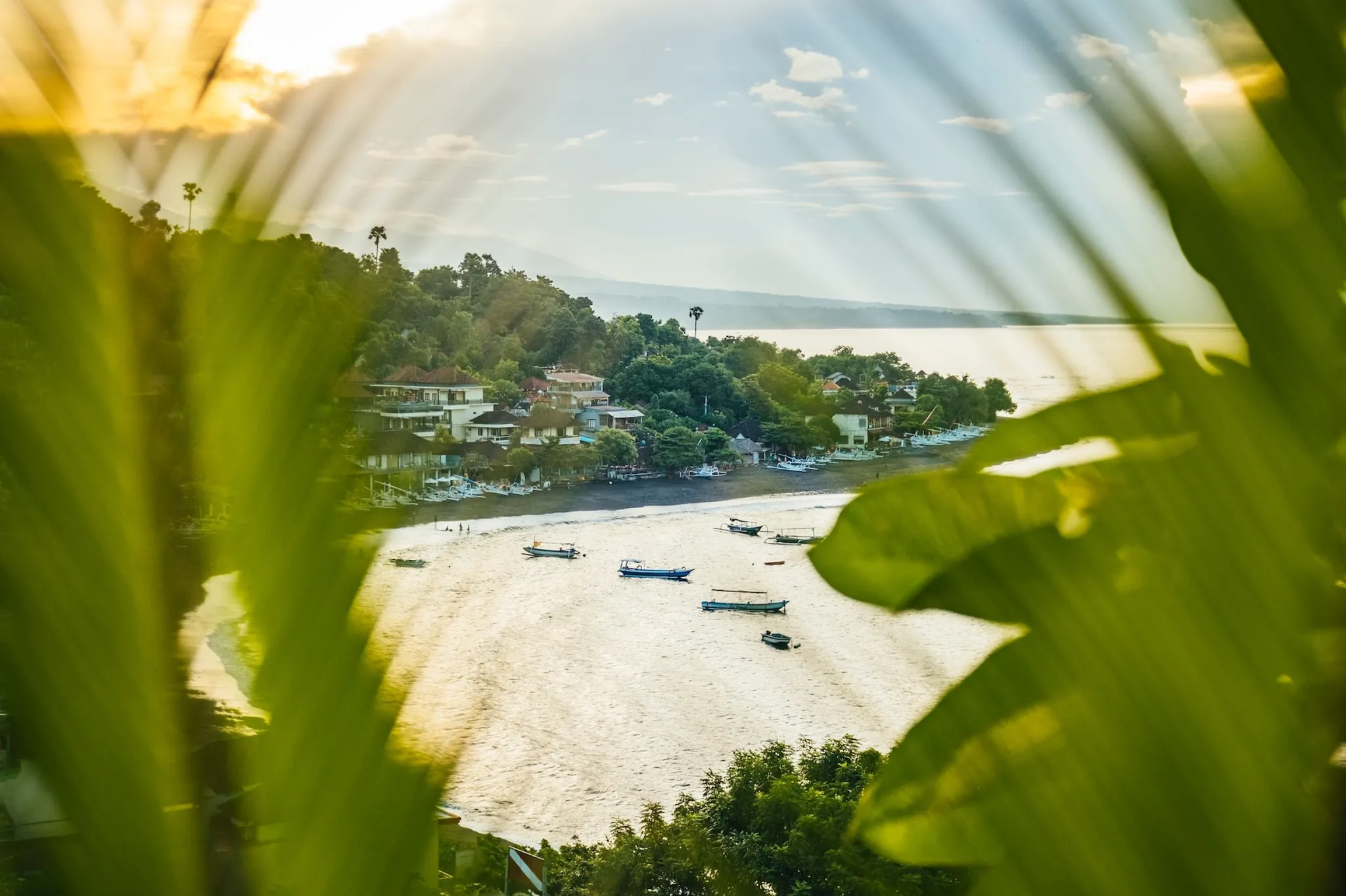 Fishing boats on a black sand beach in Amed, seen through palm leaves