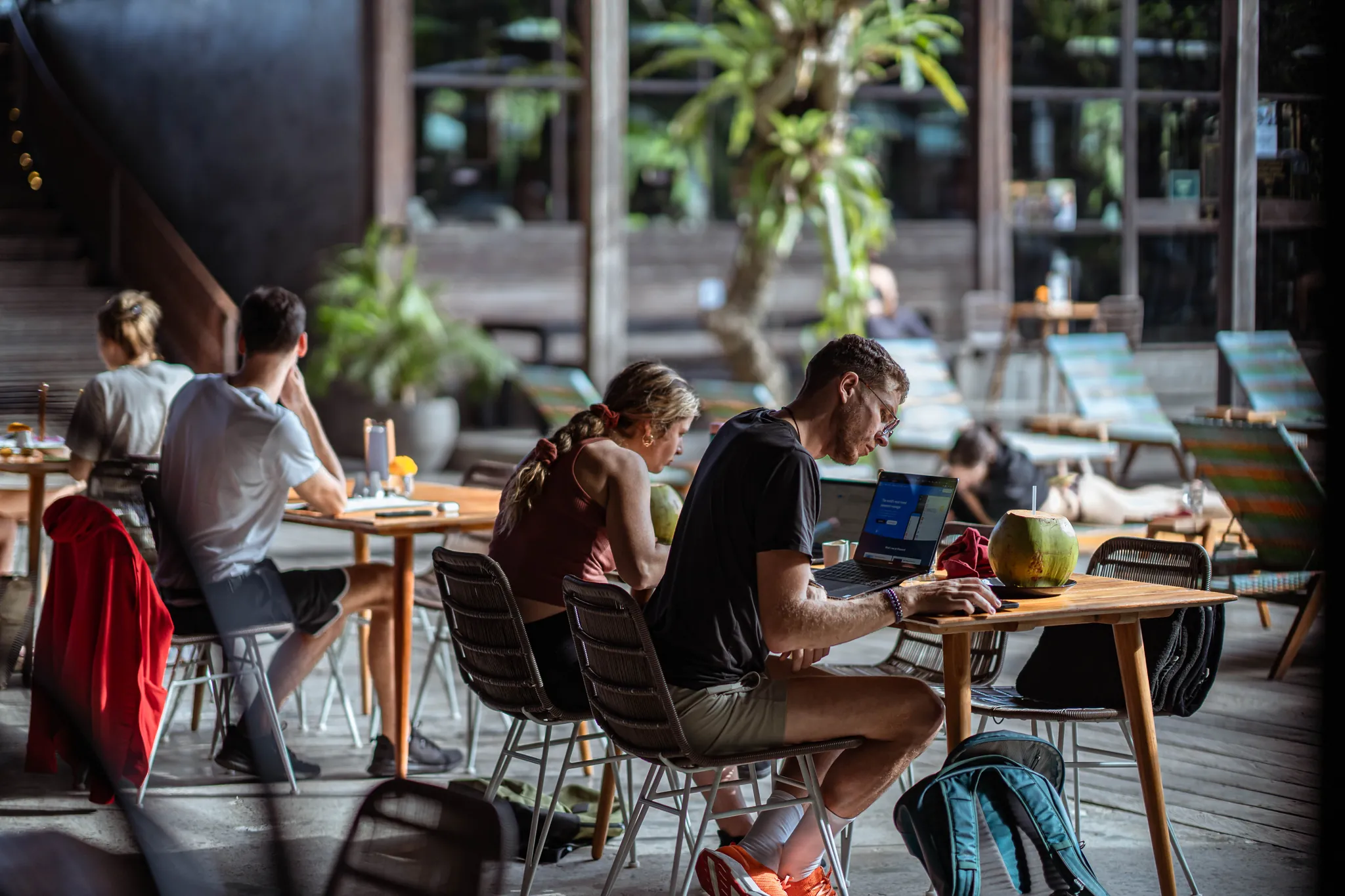 Members working on laptops at the poolside cafe tables at Titi Batu, Ubud, with sun loungers behind them